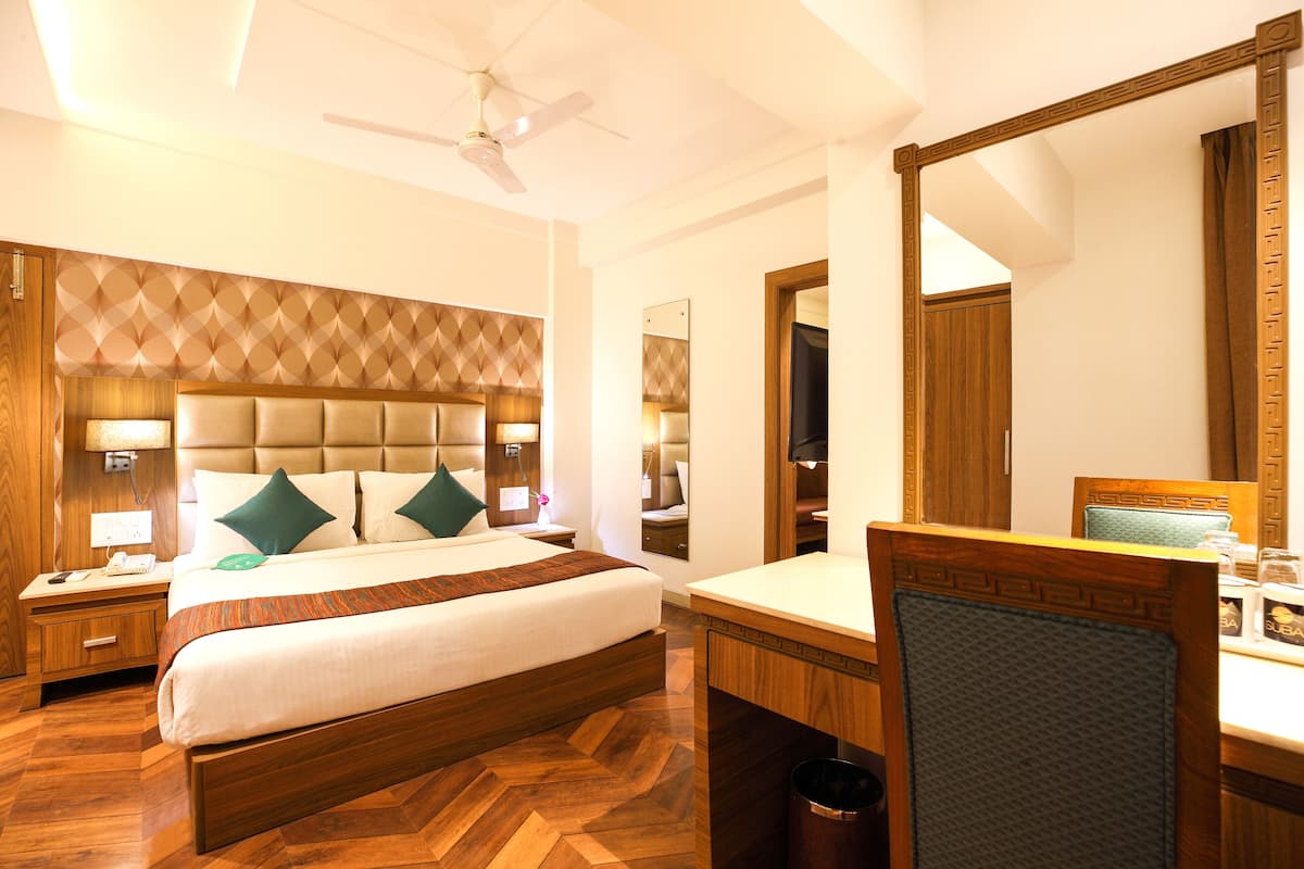 Habitación de hotel con una cama grande, cabecera de madera, una mesita de noche, escritorio, silla, espejo y un ventilador de techo.