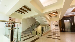 Un moderno vestíbulo de hotel con barandilla de cristal, una escalera y un ascensor.
