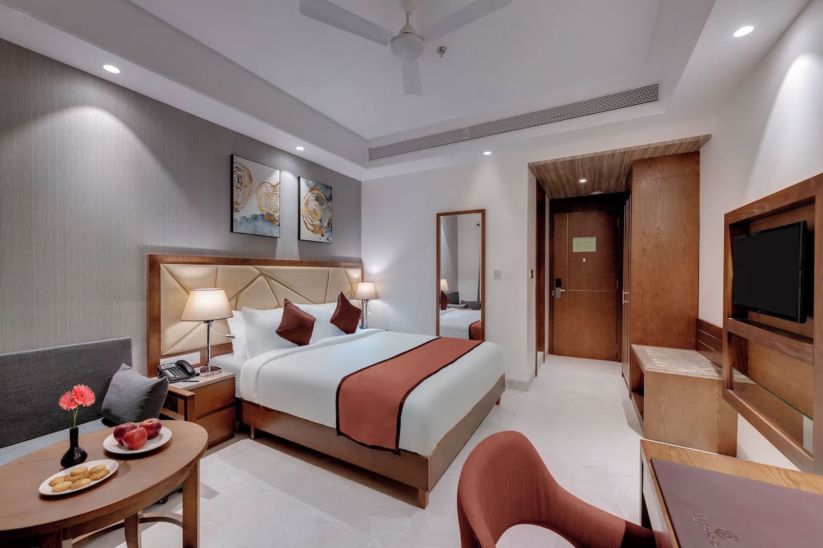Quarto de hotel com cama, mesas de cabeceira, escrivaninha, cadeira, televisão e obras de arte nas paredes.