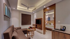 A modern hotel room with a sofa, a small table with a plate of food, a TV, and a bed with a wooden headboard. - Click Hotel Aurangabad (Chhatrapati Sambhajinagar)