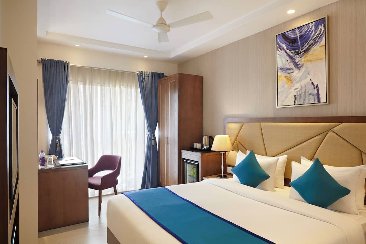 Quarto de hotel com cama, escrivaninha, cadeira, mesa de cabeceira, abajur e ventilador de teto.