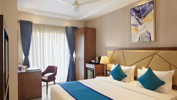 Habitación de hotel con cama, escritorio, silla, mesita de noche, lámpara y ventilador de techo.