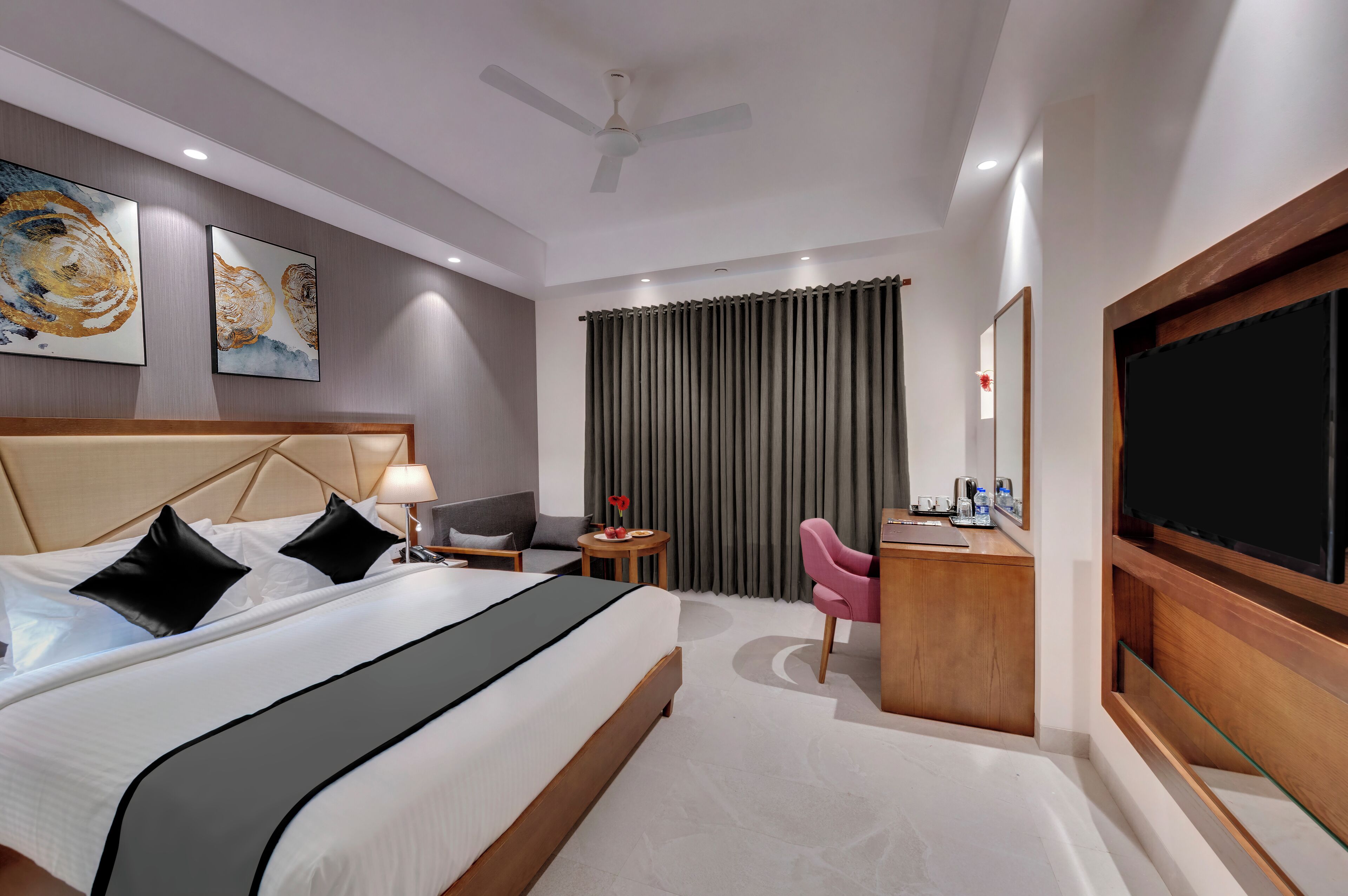 Una habitación de hotel con cama, escritorio, silla, televisor y obras de arte en la pared.