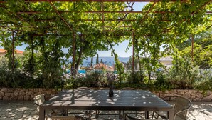 A covered outdoor dining area with a table and chairs, surrounded by greenery and a view of buildings and water in the background. - Lovely home in Novi Vinodolski (Novi Vinodolski)