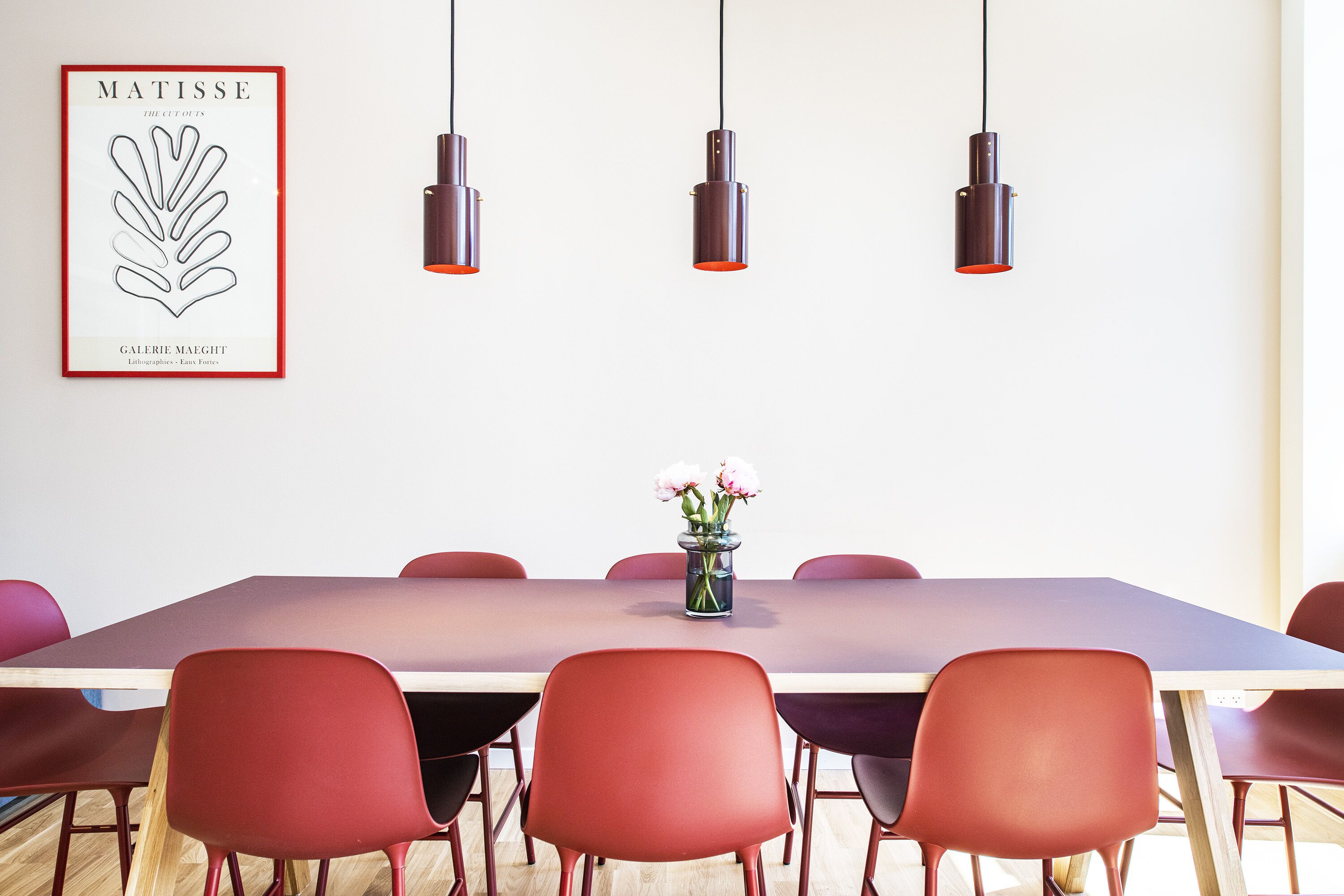 A modern dining area with a long table, red chairs, and pendant lights.