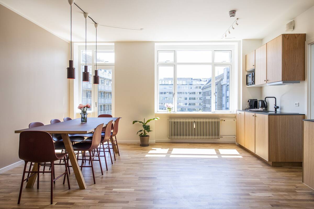 Une cuisine moderne avec des meubles en bois, une table à manger avec des chaises et une grande fenêtre donnant sur la ville.