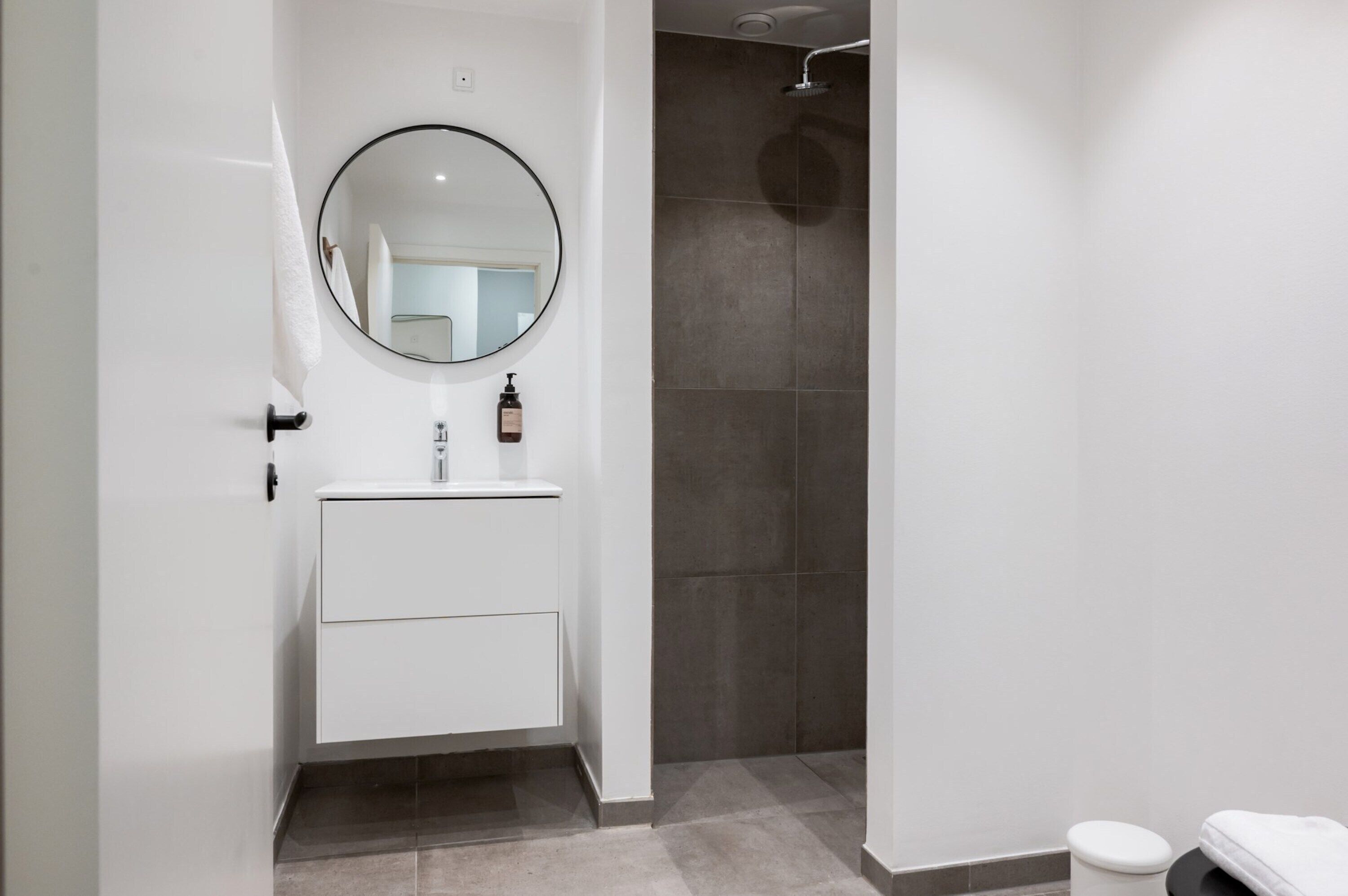 Une salle de bain moderne avec un meuble-lavabo blanc, un miroir rond et un espace douche.