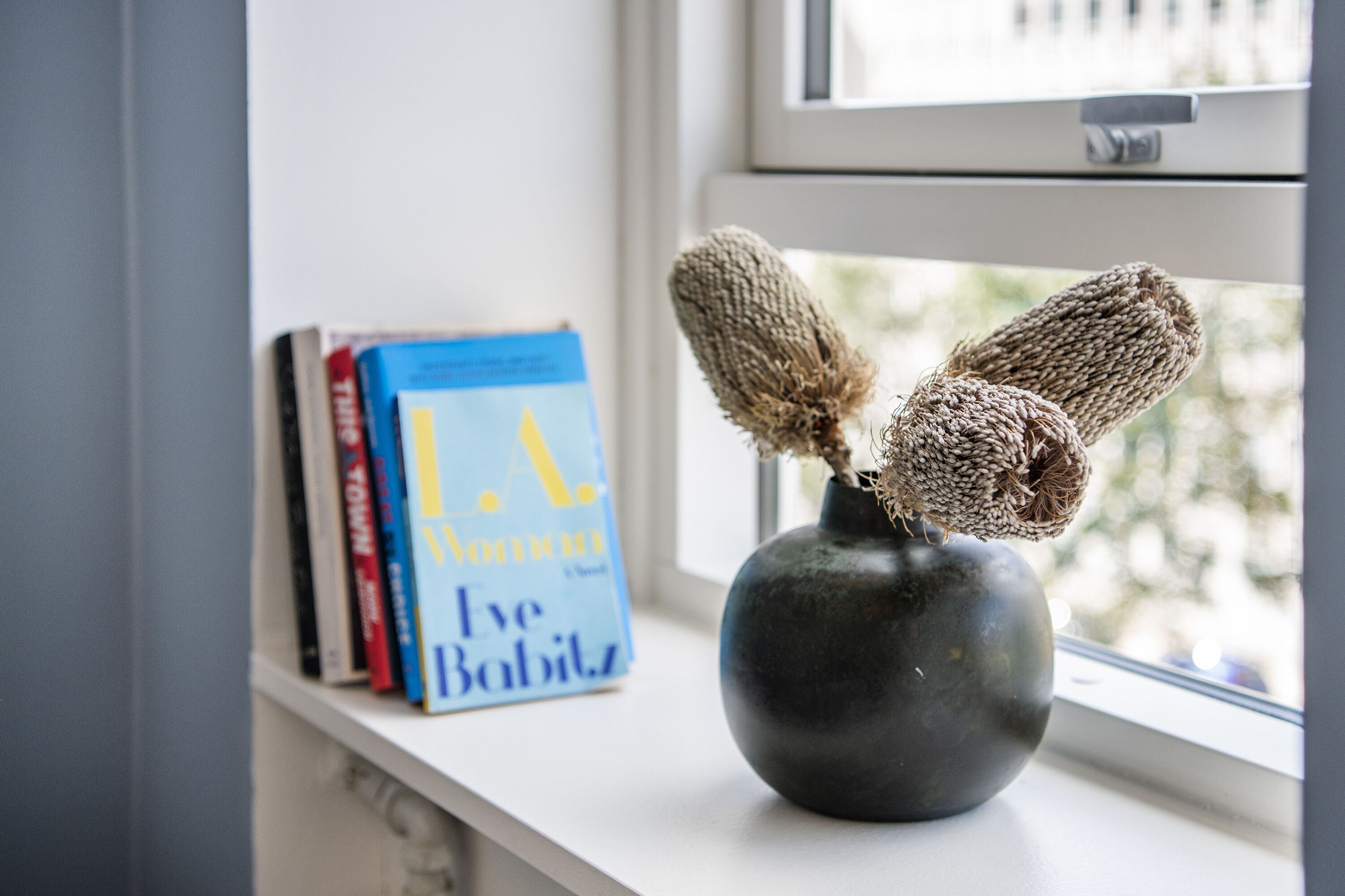 A vase with dried flowers on a windowsill next to books.