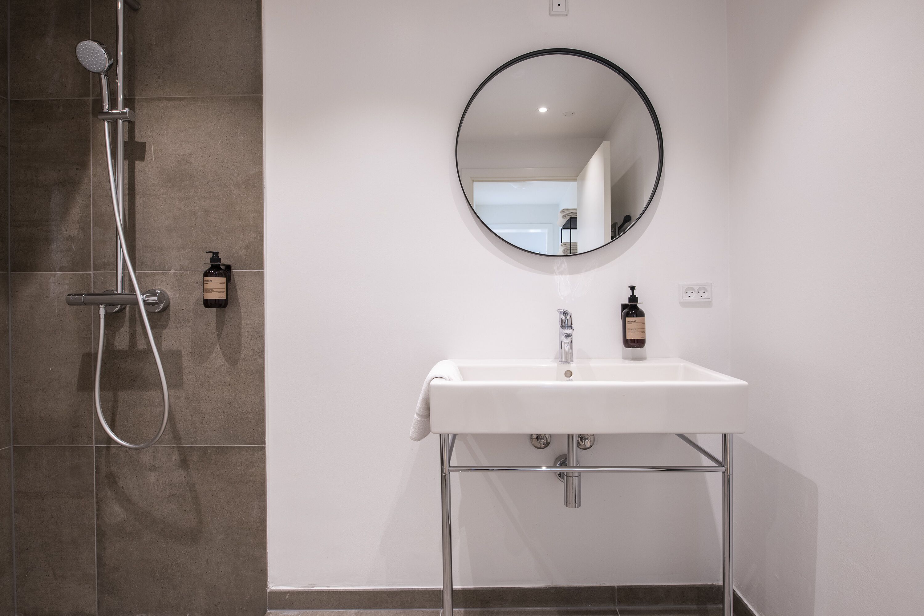 A bathroom with a shower, a sink, and a round mirror.