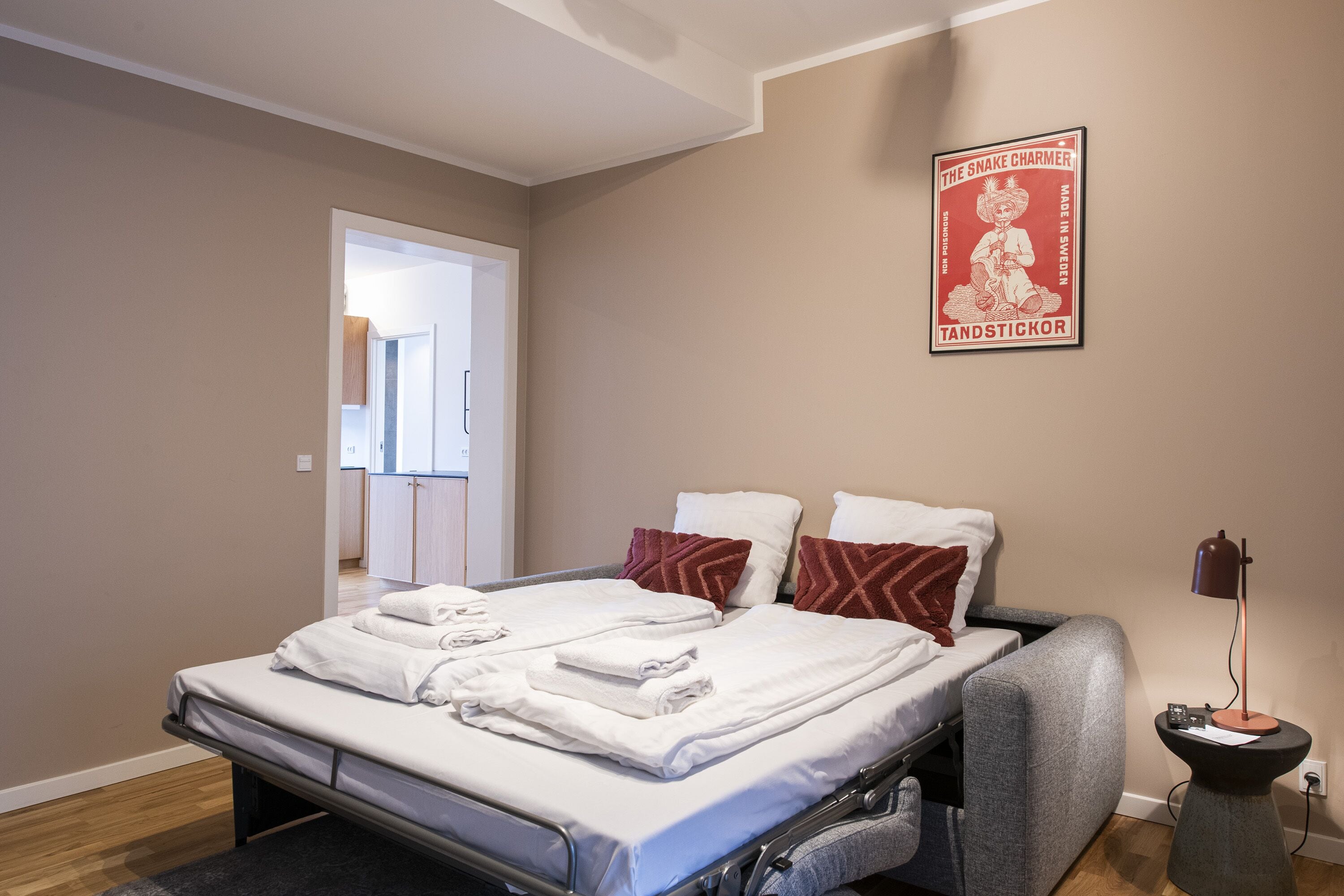 Ein Schlafzimmer mit einem Bett, Kissen, einem Nachttisch und einem Poster an der Wand.