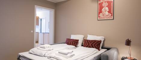 A bedroom with a bed, pillows, a bedside table, and a poster on the wall.