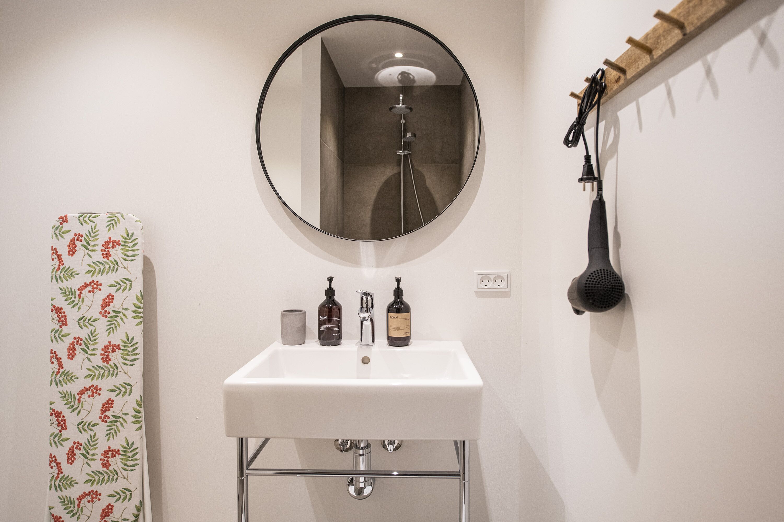 Un baño con un lavamanos blanco, un espejo redondo y un cabezal de ducha.