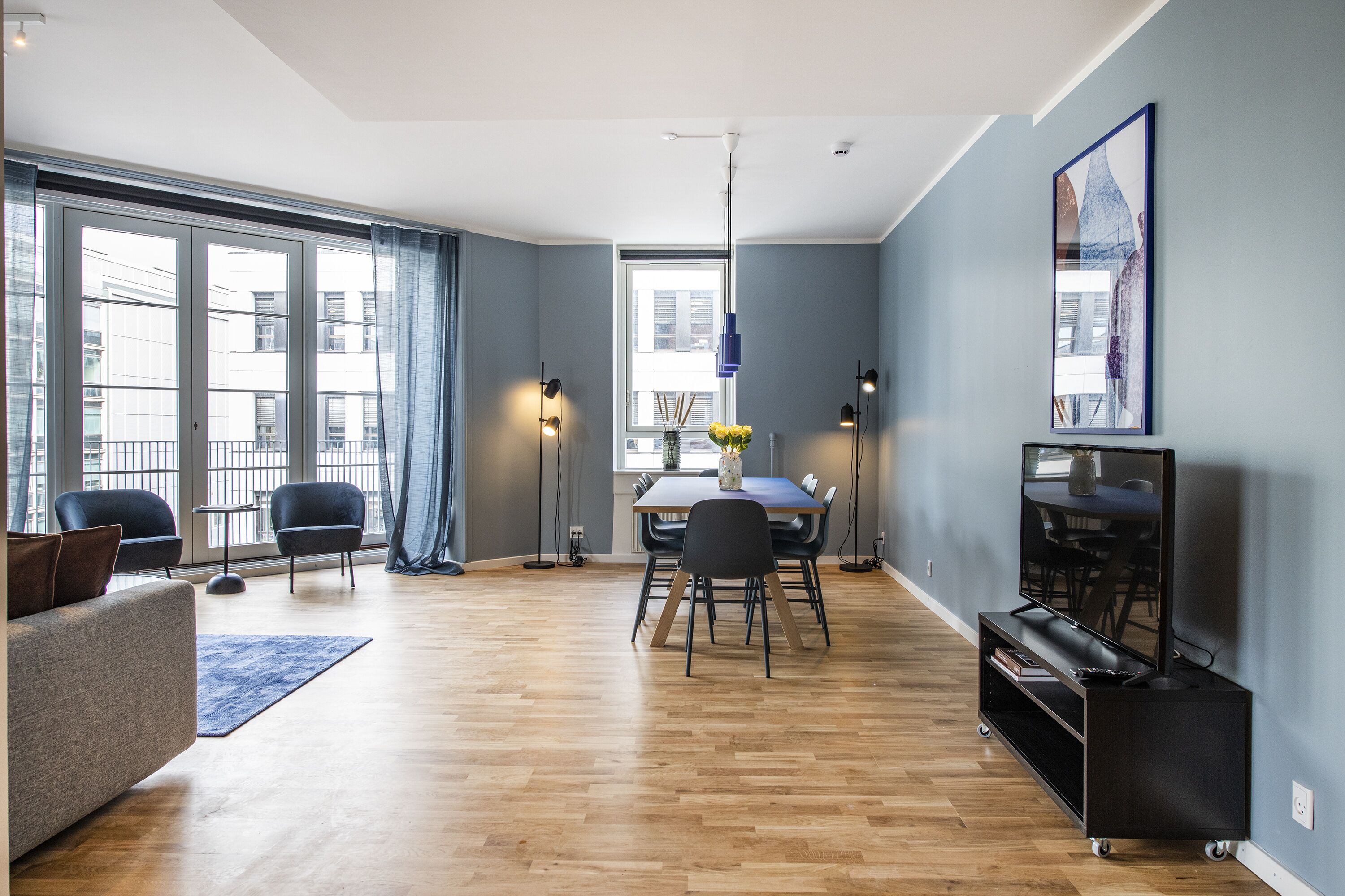 A modern living room with a dining area, large windows, and a flat-screen TV.