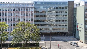 Een modern gebouw met een glazen gevel, een zebrapad en een geparkeerde auto ervoor.