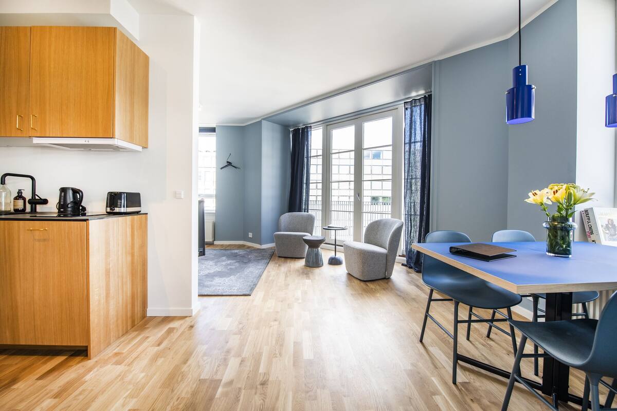 Une cuisine moderne avec des meubles en bois, une machine à café et une bouilloire. On y trouve également un coin repas avec une table, des chaises et un vase rempli de fleurs.