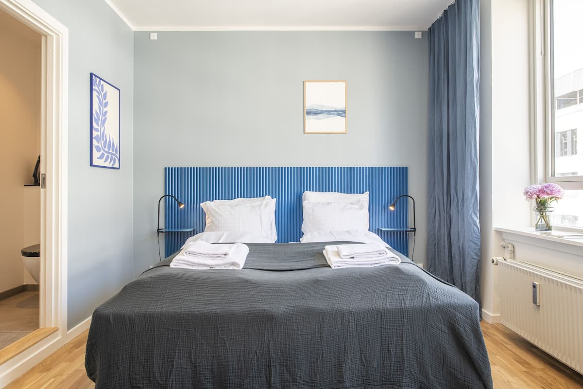 Une chambre d’hôtel avec un lit, deux tables de chevet, une fenêtre avec des rideaux et un tableau encadré au mur.