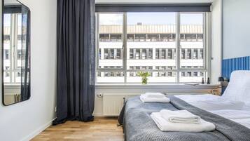 Et hotelværelse med et stort vindue, en seng med pænt foldede håndklæder, en radiator og en potteplante på vindueskarmen.