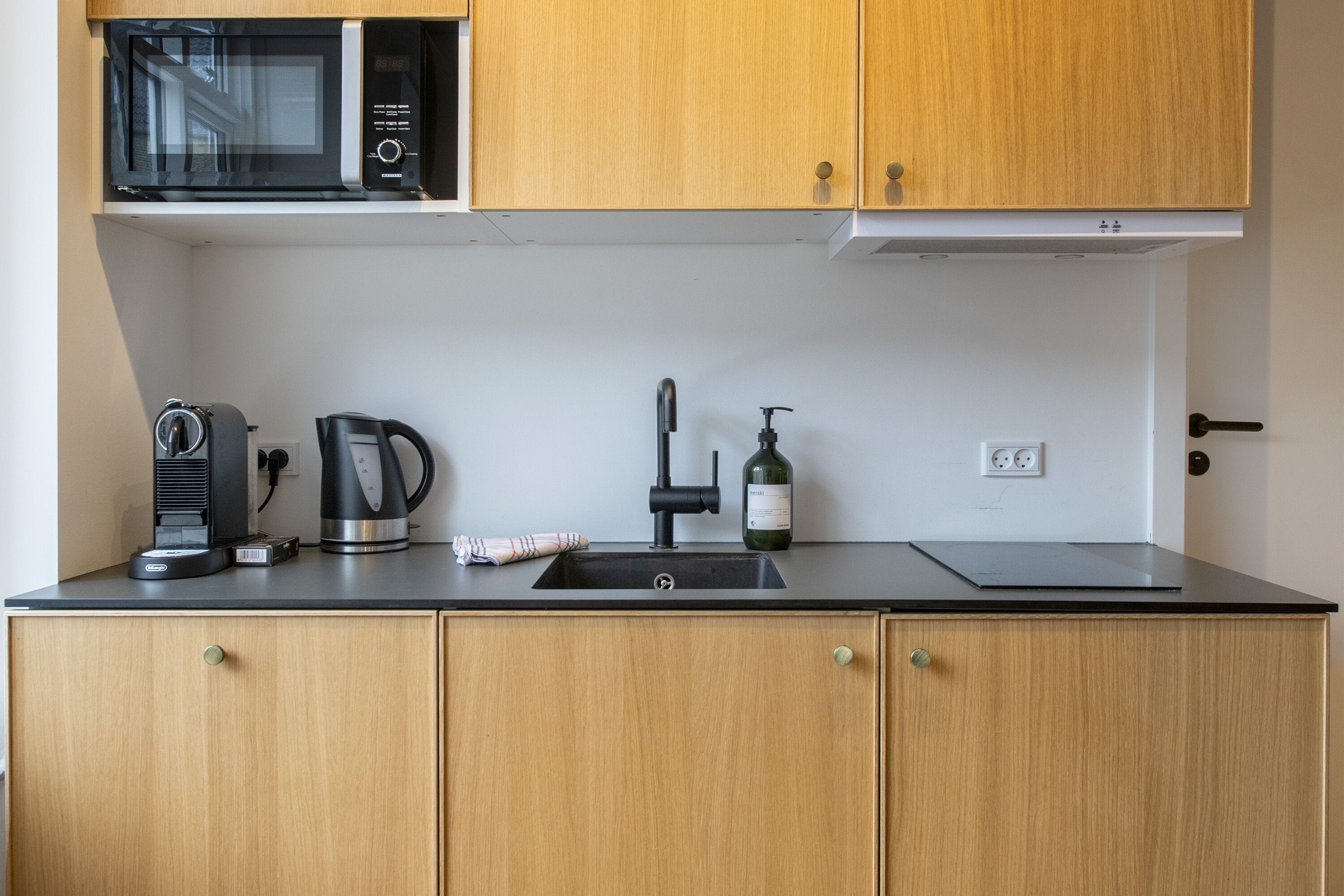 A kitchenette with a microwave, coffee maker, kettle, and wine bottle.