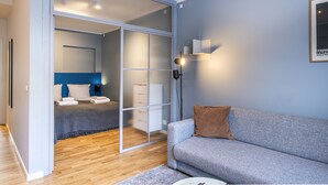 Een moderne slaapkamer met een schuifglazen deur naar een badkamer, een grijze bank en een wandlamp.