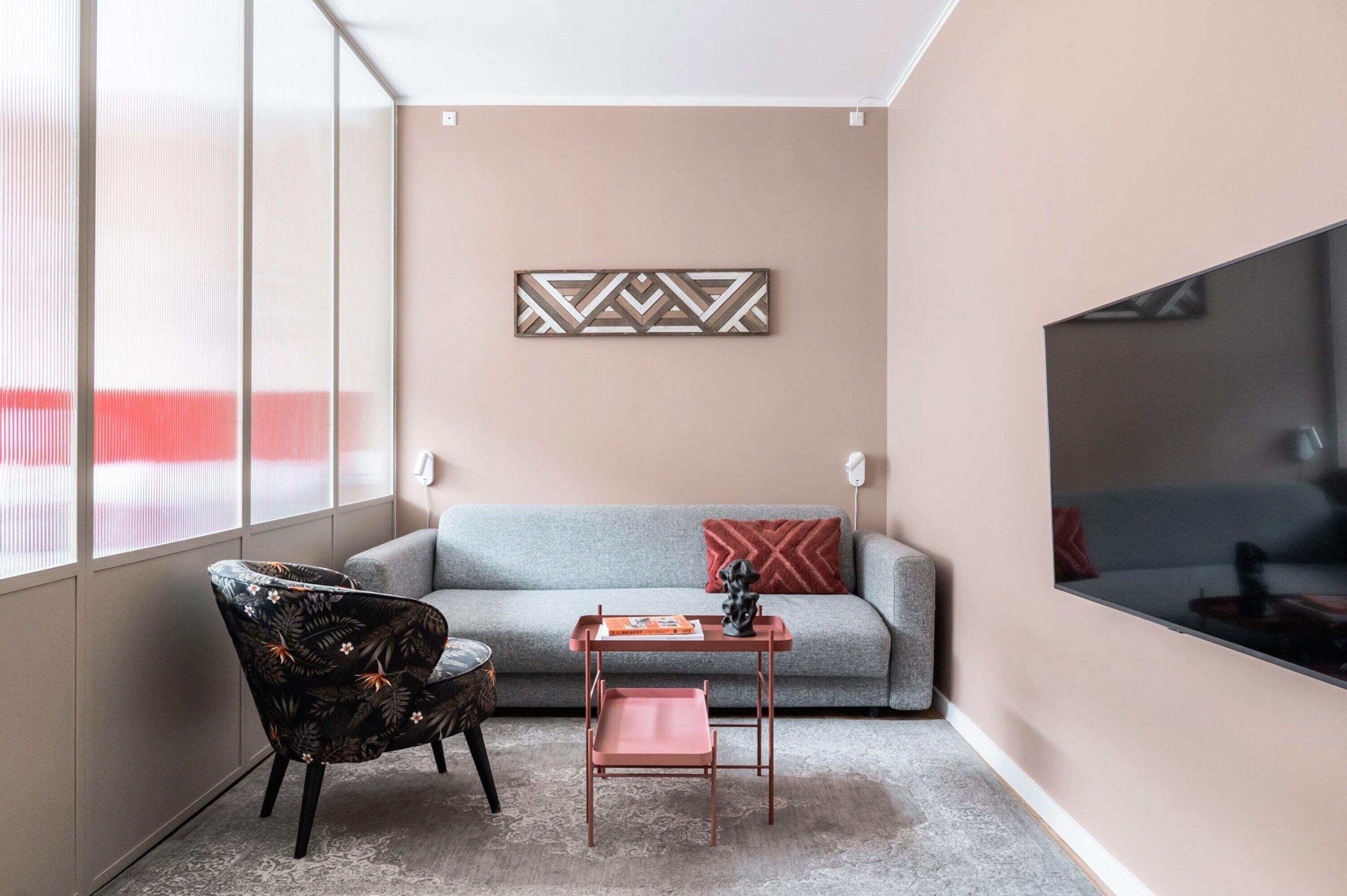 A modern living room with a grey sofa, a patterned armchair, a small wooden table, and a decorative wall piece.