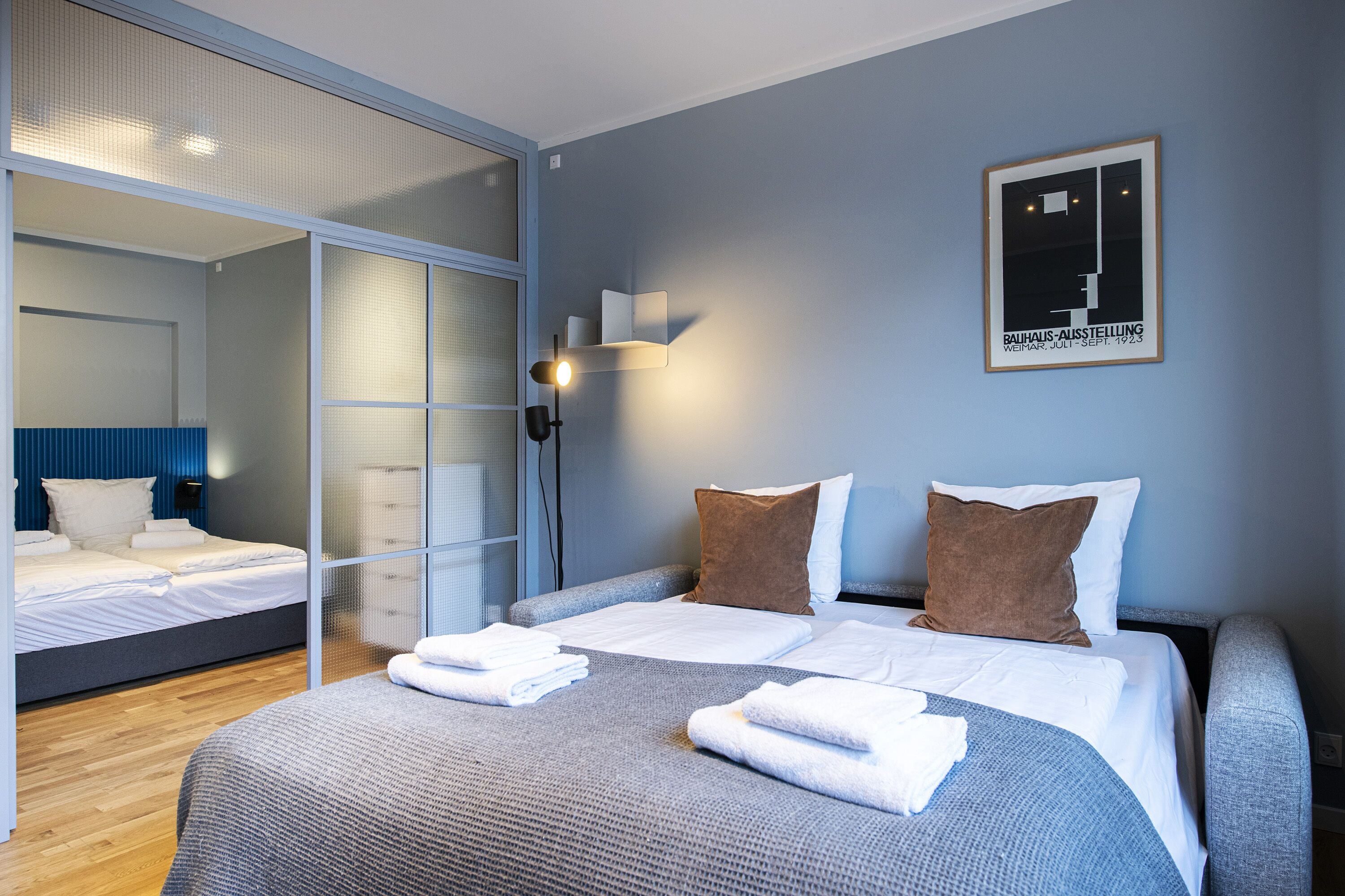 Une chambre d’hôtel moderne avec un grand lit, un lit plus petit et une cloison en verre.