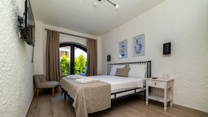 A bedroom with a bed, a chair, a bedside table, and a TV mounted on the wall. - Cemal Alaçatı Hotel (Cesme)