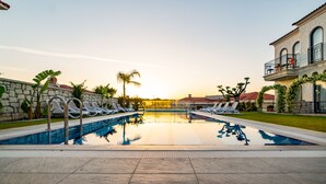 A swimming pool with lounge chairs, a stone wall, and a building with a balcony. - Cemal Alaçatı Hotel (Cesme)
