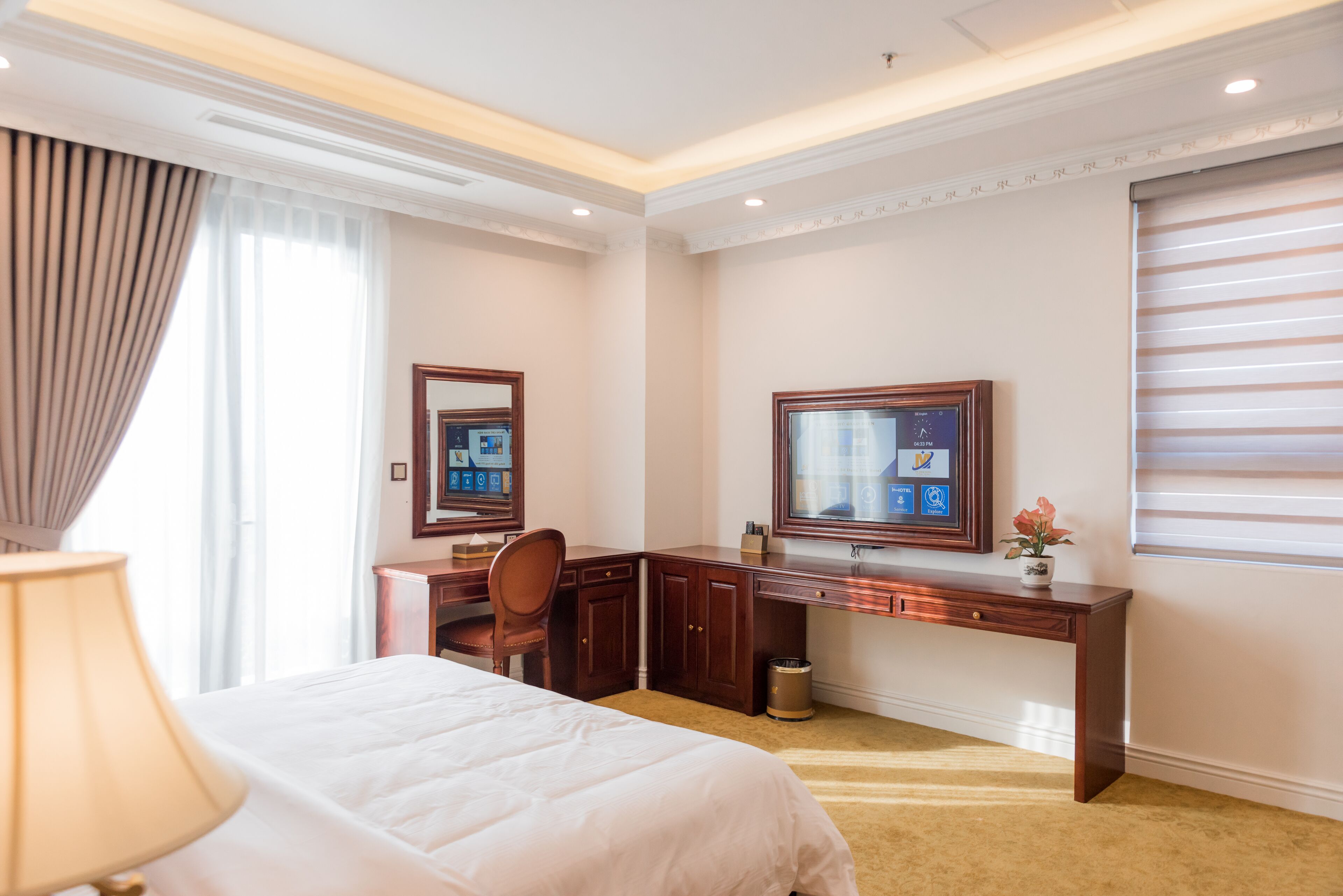 A hotel room with a bed, desk, chair, TV, and a window with blinds.