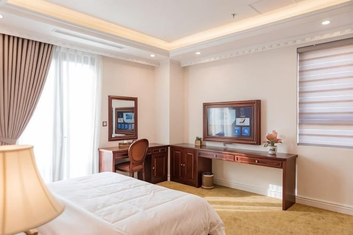 A hotel room with a bed, desk, chair, TV, and a window with blinds.