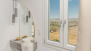 Ein Badezimmer mit einem großen Spiegel, einem Waschtisch mit einer Teller Kekse und Blick auf eine ländliche Landschaft durch ein Fenster.