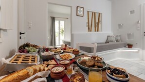 Ein reichhaltiges Frühstücksbuffet mit Speisen und Getränken auf einem Tisch in einem hellen Raum, der eine Couch und ein Fenster zeigt.