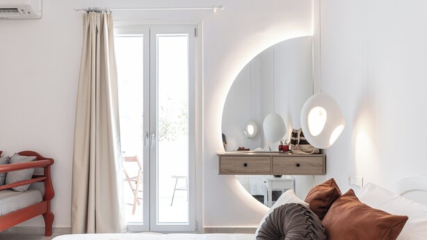 Ein Schlafzimmer mit Bett, Nachttisch mit Spiegel, Kommode und einem Fenster mit Vorhängen.