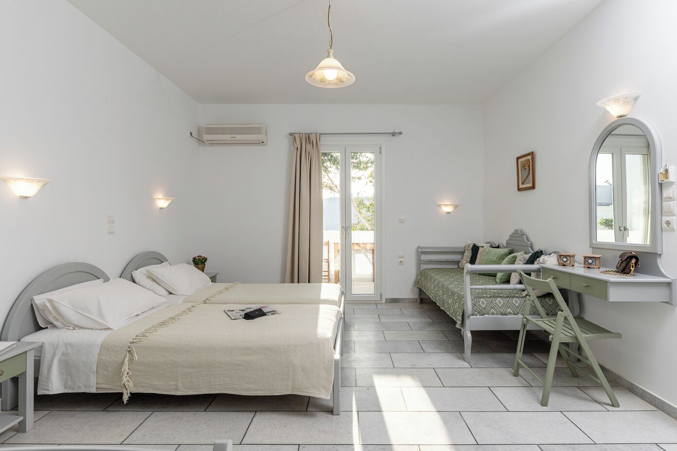 Une chambre avec deux lits, un bureau, une chaise, un miroir et une porte-fenêtre donnant sur un balcon.