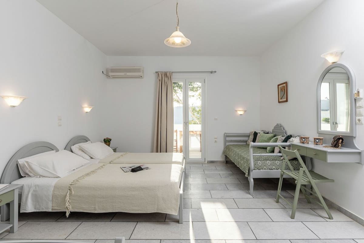 A bedroom with two beds, a desk, a chair, a mirror, and a balcony door.