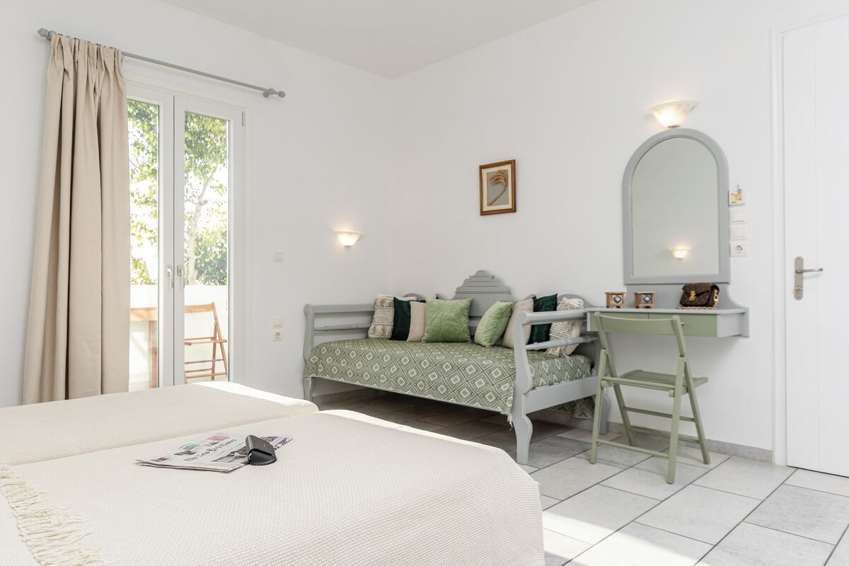 A bedroom with a bed, a desk, a chair, a mirror, and a door.