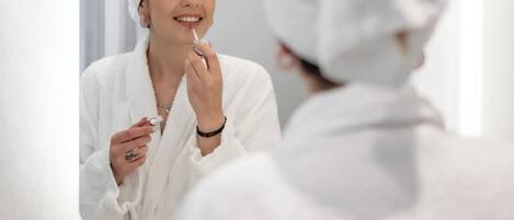 A person in a white bathrobe with a towel wrapped around their head, standing in front of a mirror.