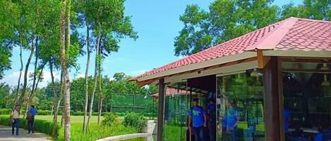 A glass-enclosed pavilion with a red roof, surrounded by a landscaped garden and a small pond.