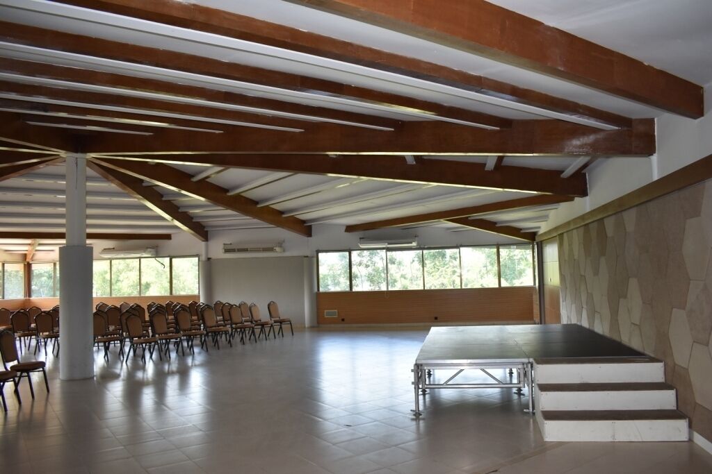 A spacious hall with a high ceiling, wooden beams, a stage, and rows of chairs.