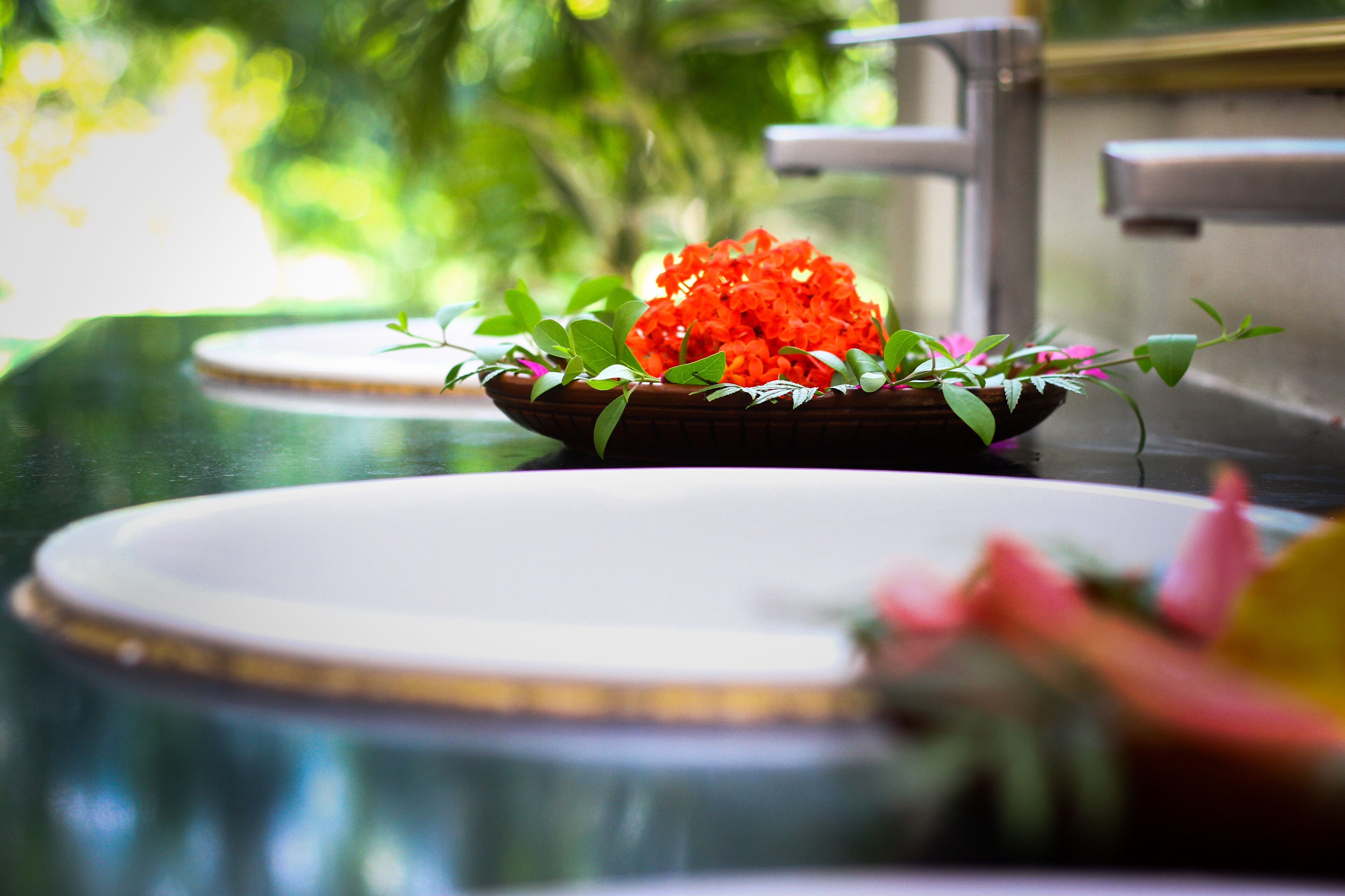 A bowl of red flowers on a white countertop with a green cloth underneath.