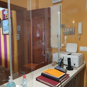 Una habitación de hotel con escritorio, impresora, teléfono y un separador de vidrio.