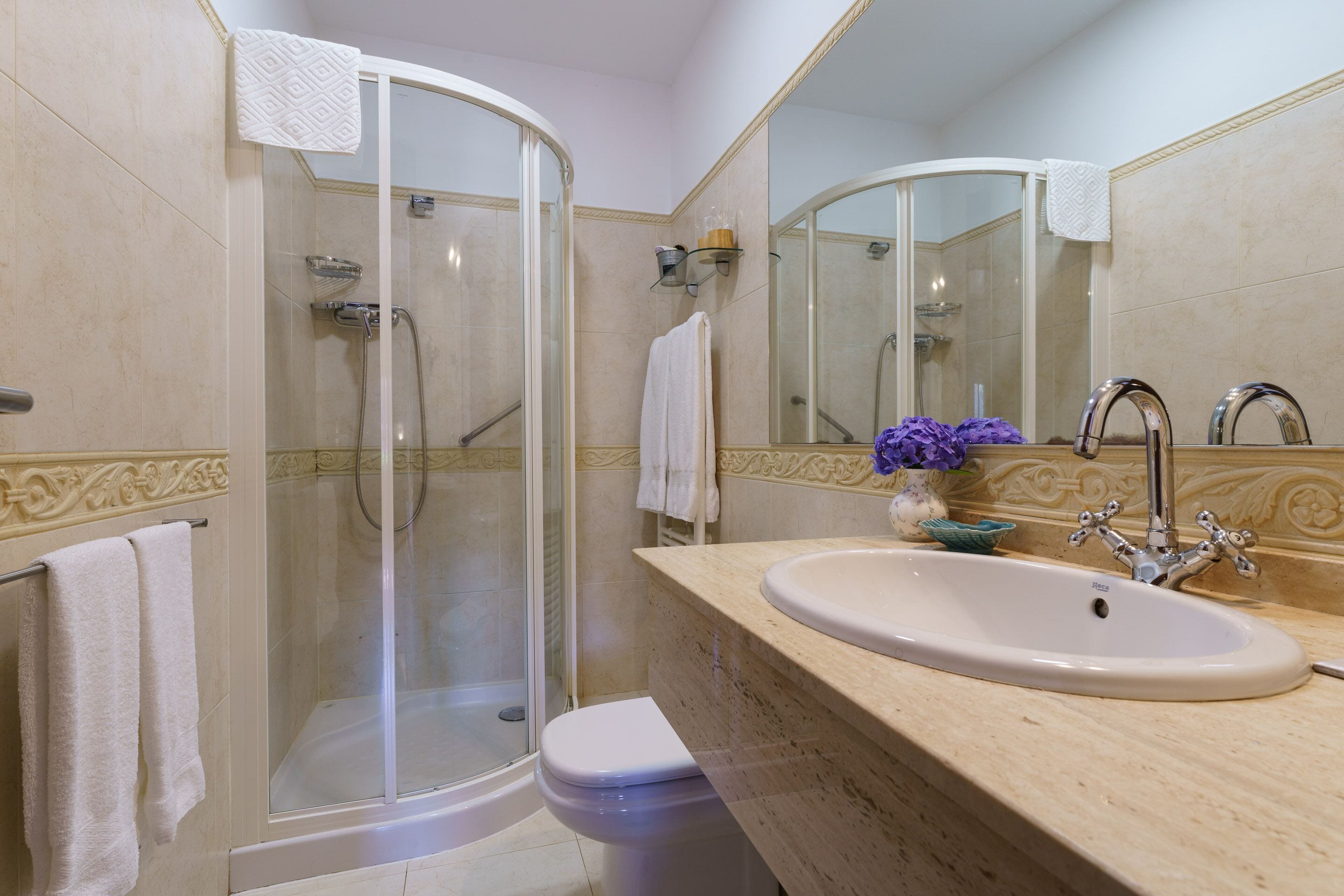 Een badkamer met een glazen douchecabine, een wit toilet, een wastafel met spiegel en decoratieve tegels.