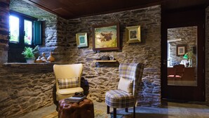 A cozy room with stone walls, two chairs, a leather ottoman, and a window with a view.