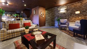A cozy lobby with a wooden ceiling, a stone wall, and a mix of seating including a plaid sofa and armchairs.