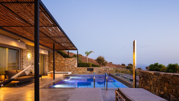 Un área de piscina moderna al aire libre con una pared de piedra, un pérgola de madera y vistas al paisaje.