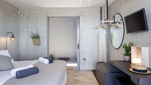 Una habitación de hotel moderna con cama, mesita de noche, televisor y un pequeño escritorio.