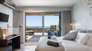 Habitación de hotel moderna con una cama grande, un escritorio y vistas al mar a través de un ventanal corredero.