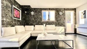 Un salon moderne avec un canapé d’angle, une table basse blanche et un vase rempli de fleurs.