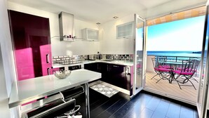 Une cuisine moderne donnant sur la mer, avec une porte coulissante vitrée qui s’ouvre.