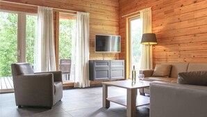 A cozy room with wooden walls, a flat-screen TV, a sofa, a coffee table, and a dining table. - Lovely home in HEEL with lake view (HEEL)