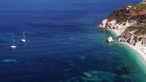 A coastal area with clear blue waters, a sandy beach, and rocky cliffs.